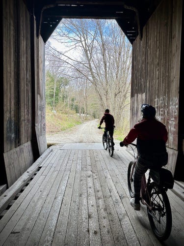 two people emerging from an old covered railroad bridge made mostly of heavy lumber