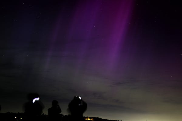 Silhouettes of people taking photos of the northern lights on parliament hill in London