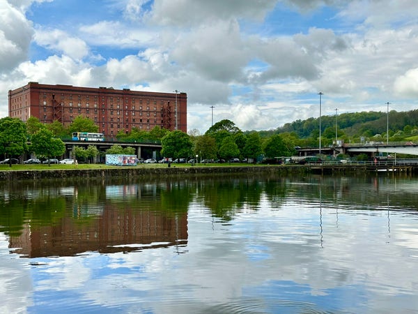 Photograph of Cumberland Basin, with one of the red brick bonded warehouses in the background. The sky is reflected off the water.