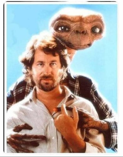 Okay, so Stephen Spielberg is standing with E.T. behind him, but despite the fact the E.T. is short he looks a head taller than Stephen. The picture has the haziness of a glamor photo, and looks like the kind of picture two gay innkeepers who live in Maine would take to put in the lobby of their inn. E.T. is wearing a flannel shirt, Stephen is wearing a white button up. Both of E.T.'s arms are around Stephen and Stephen is holding one of E.T.'s fingers. 
