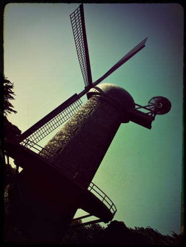 A green-tinted retro view of the tall, wooden Dutch Windmill in Golden Gate Park, near Ocean Beach.

The windmill, mostly silhouetted, is tilted in this picture, leaning back as the setting sun illuminates the western face.