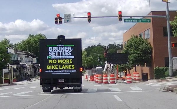 A billboard truck reading, "Margo Bruner-Settles / City Council / No More Bike Lanes" in the middle of an intersection, with the traffic light red.