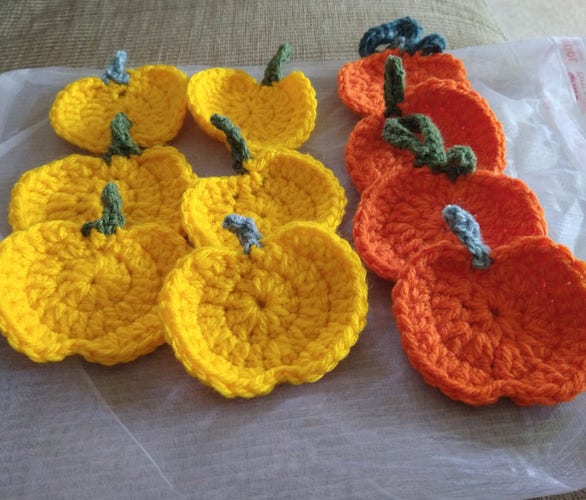Six small yellow crochet pumpkins with green stalks, on the right are four bright orange crochet pumpkins with green stalks 