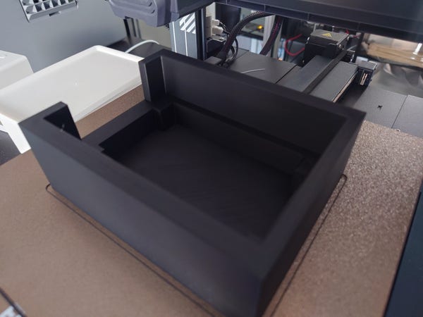 A 3D printed tray, in black, still on the printer's bed.