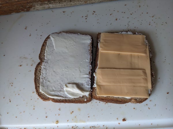 two pieces of bread; one is slathered with mayonnaise, and the other is topped with kraft singles.