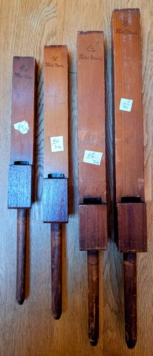 Four antique wooden church organ pipes, increasing in size from left to right. Each one is a square box with a small opening near the bottom, on top of a dowel.