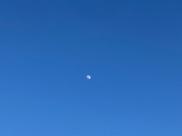 Komplett wolkenfreie hauchzart diesiger azurblauer Himmel. Genau in der Mitte schwebt der zunehmende Dreiviertelmond.