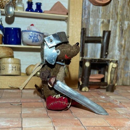 Photo of Silvius, the baby Latin mouse, trying out Minimus' army equipment. He's wearing a helmet that is far too big for him, and he can't lift the sword, but he is smiling happily. As long as he doesn't drop the sword on his little toes...