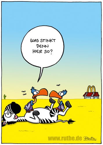 Zwei Geier in der Wüste sitzen auf einem vergammelnden Kadaver. Linker Geier zum Rechten: "Was stinkt denn hier so?". Im Hintergrund sehen wir eine Filiale von McDonald’s.