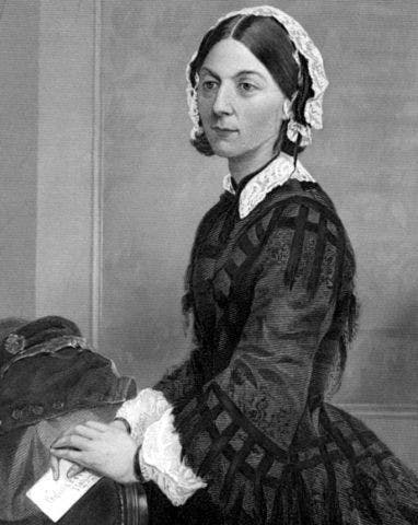 Image en noir et blanc de Florence Nightingale assise, portant une robe victorienne détaillée et un bonnet blanc. Elle tient un livre ouvert dans sa main droite.