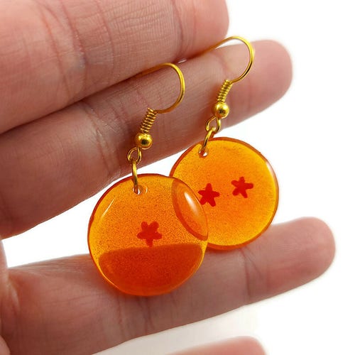 Boucles d'oreilles pendantes en forme de boules de cristal tirées du manga Dragon Ball.
Éco-responsables, elles sont réalisées en CD recyclé peint à la main, puis recouvertes de résine époxy BIO teintée orange.