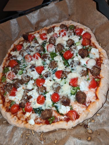 a pizza with meatballs, spinach, half cherry tomatoes, green onion, and cheeses on a tomato sauce base