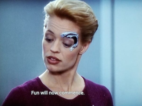 Voyager scene. Seven of Nine (tertiary adjunct of unimatrix 01) is pictured. She has a metal robotic implant around her left eye because she is a borgs. Closed caption reads, "Fun will now commence."