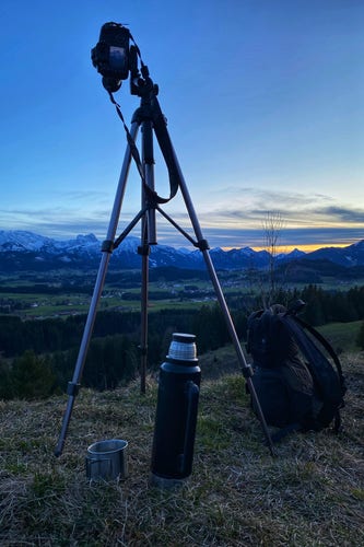 A tripod, thermos and backpack are overseeing the Allgäuer Alps and its preceding hills during sunset