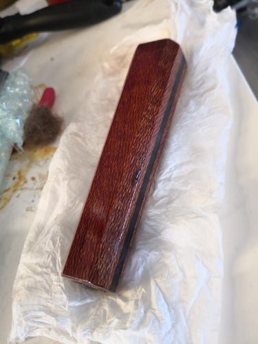 A knife handle being oiled. It's a octagonal shape, and a red brown colour there's a very tight, complex pattern it the wood