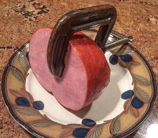 A G-Clamp is clamped onto a ham sitting on a plate. 