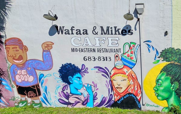 The side of a popular Cafe decorated with mural style images of a variety of individuals if differing backgrounds, representing the diversity of the neighborhood.
