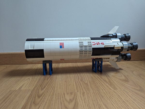 Lego 21309 NASA Apollo Saturn V first stage lying on two small blue stands. Mainly white, we ca see its reactors on the right.