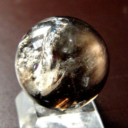 A small polished sphere on a stand, half of it is clear quartz and a wavy line divides it from a smoky side, streaked with shadow.