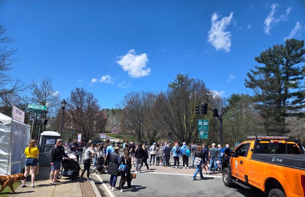 Crowds lining the side of the road for the Boston Marathon, with some of the runners visible through the crowd, on a bright sunny day
