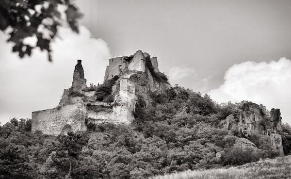 Black and white photo of a ruined castle perched atop a rocky hill surrounded by trees.