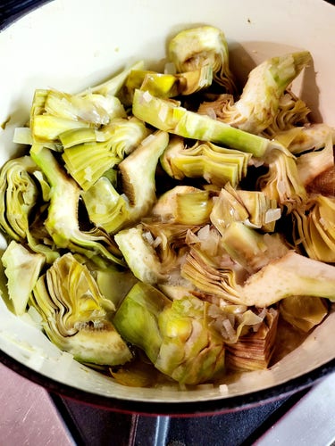 A pot simmering with trimmed artichokes, shallots, and white wine. 
