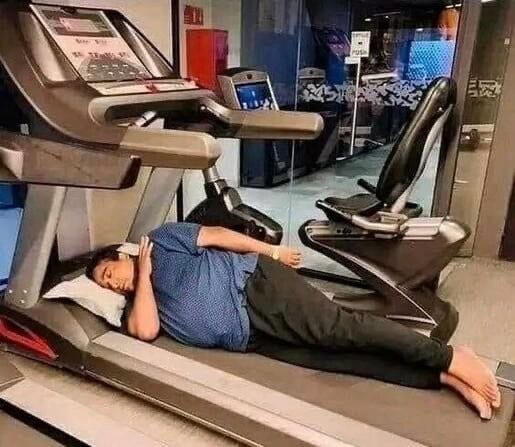 Photo of someone sleeping on a treadmill with a pillow. 