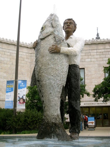 statue of a man hugging a fish the same height as him

he looks up as though their intimate embrace was witnessed unexpectedly