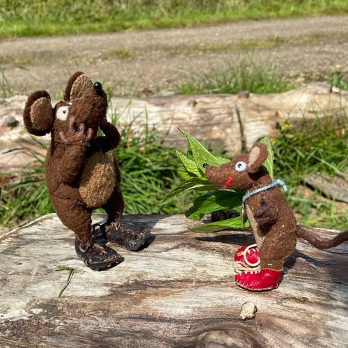 Photo of Minimus and Silvius, the Latin mice, standing on a log. Silvius is brandishing a sprig of mint at Minimus, who jumps back in fear. Does Silvius not realise that mice are repelled by the smell of mint?