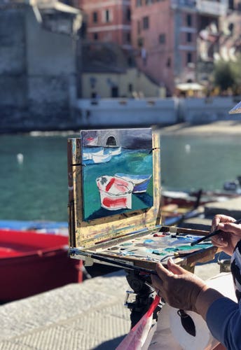 A woman painting the small harbour with a red boat and turquoise water in the early morning