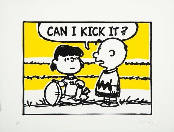 Lucy holding the ball for Charlie Brown with the caption Can I Kick It