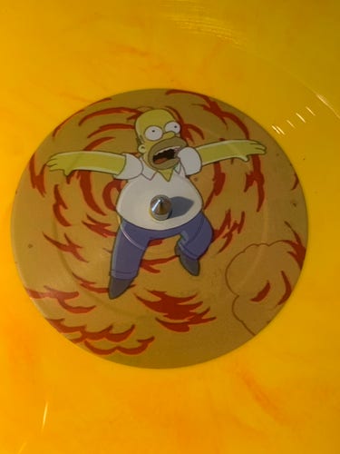 A photo of a record where the centre label is an image of Homer Simpson in what appears to be an explosion. The centre hole for the spindle is perfectly aligned with where his belly button would be 