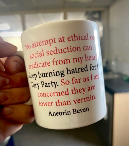 A hand holding a mug which bears a quote from former Labour MP Aneurin Bevan. The quote says:

“No attempt at ethical or social seduction can eradicated from my heart a deep burning hatred for the Tory Party. So far as I am concerned they are lower than vermin”