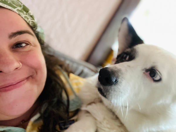 Brunette in a yellow fleece, smiling, and a corgi who just had dinner and is laying on her chest, politely - for now - asking for second dinners. Which he will not get. Because despite his stature, he is not a hobbit. 