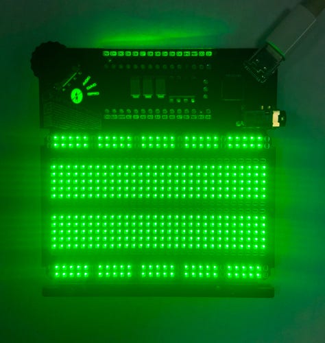 Jumperless V5 lit up in green. Note the backlit text on the HASL pads labeled ADC, DAC, and GPIO because I think it's fucking rad, those are meant to be touched with the probe to connect them to the breadboard.