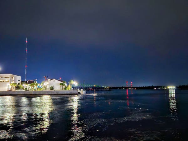 From the north ending point of the downtown Riverwalk,  a late night view across the mouth of a small creek emptying into the Saint Johns River with colorful business skyline in the distance.
