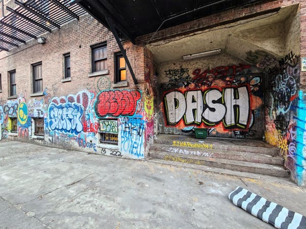 Colorful graffiti with bubble letters and bubble words across the rear of an old downtown brick building from the dirty alleyway behind.  One identifiable word is "Dash," possibly the graffiti artist's name?