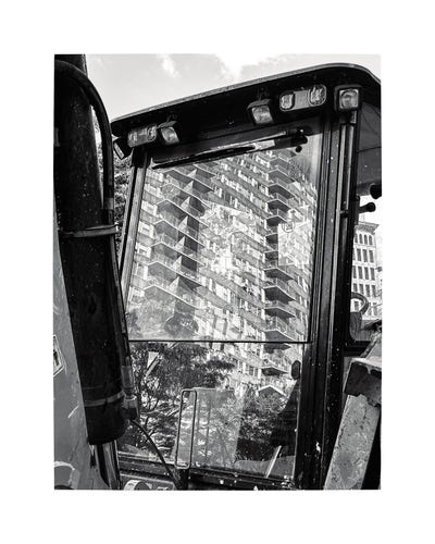 A large co-op apartment building reflected on the windshield of a parked backhoe in Manhattan. 