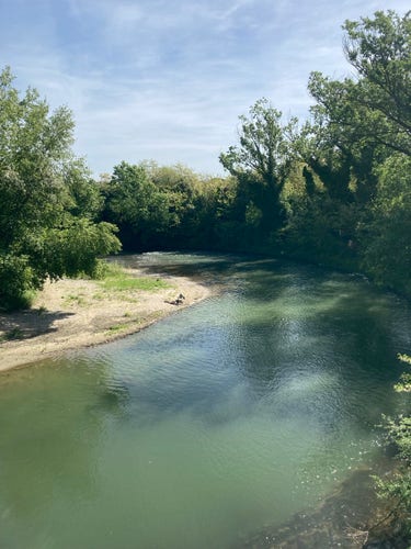 A lazy bend in the Tiber River on a sunny morning. A lone fisherman is setting up on the left bank. Trees line both sides of the river. #Umbria