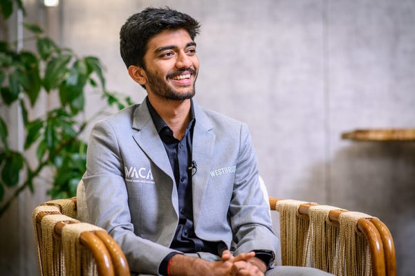 Gukesh sits on a chair, smiling. (Picture: FIDE / Michal Walusza)