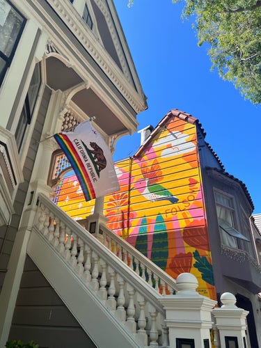 a mural of a hummingbird and flowers on a house next to a california rainbow flag