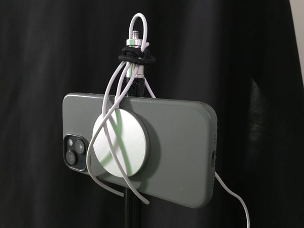 An iPhone 14 held onto a tripod using a MagSafe charger, some creative running of the charger's cable, and two hair ties.