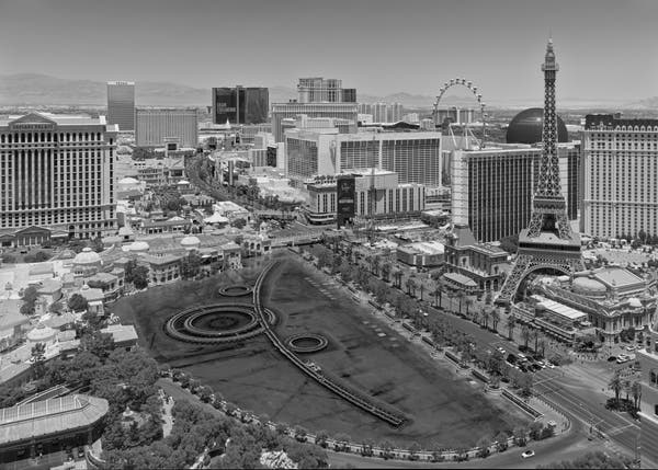 Las Vegas Strip, looking north from a high vantage point during the day. Among the hotel buildings is fake Eiffel Tower, a creepy sphere, a ferris wheel, and large, idle fountain in foreground. There is no empty space anywhere.