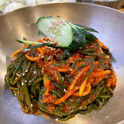 Pikantne koreańskie danie z makaronu z warzywami i sezamem, podawane w metalowej misce.