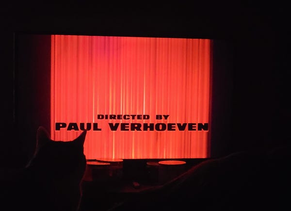 Directed by Paul Verhoeven. The intro of Total Recall, black text on red background, on my TV in a dark room. Cat head in the way. 