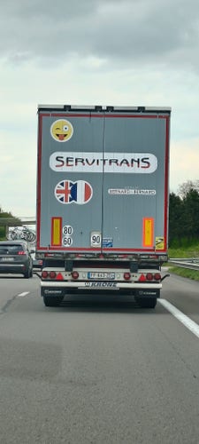 Picture of the back of a "Servitrans" truck driving on the highway. There's a 😜 emoji on top of the logo