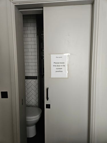 Bathroom door in hotel room a quarter open, with a printed sign "Please leave the door in its current position."