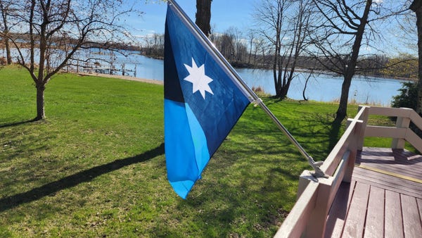 Against the backdrop of a Minnesota lake, the new Mn flag hangs on a pole.