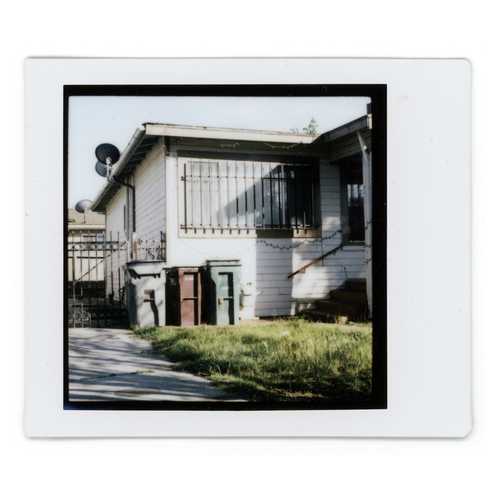 Instax photo of a house and three garbage bins.
