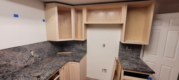 Half a kitchen with cabinets without doors, marble countertop in place.